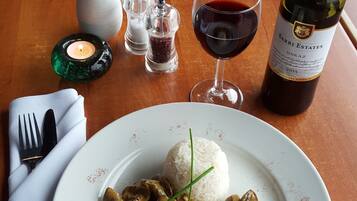 A dining table with a plate of mushroom risotto, a bottle of wine, and a vase with flowers.