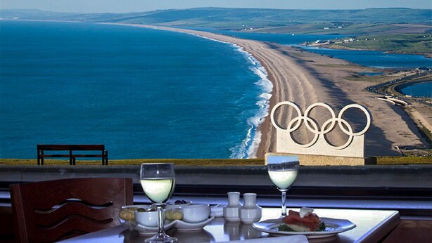 Une table offrant une vue sur une plage et la sculpture des anneaux olympiques.