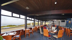Un restaurant offrant une vue sur l’eau, avec des tables et des chaises en bois, et un décor intérieur moderne.