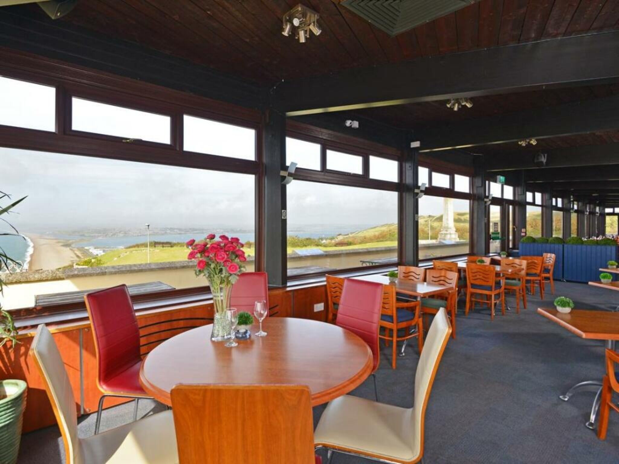 A restaurant with a view of the coastline, featuring round tables and red chairs.