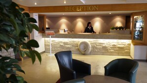 Un espace d’accueil comprenant un comptoir de réception, deux chaises, une table ronde et un panneau indiquant « RÉCEPTION ».