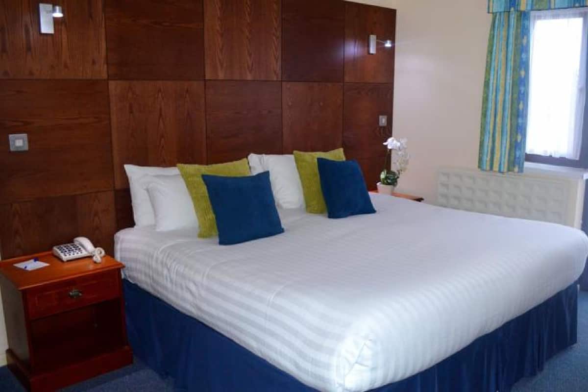 A hotel room with a large bed, a bedside telephone, and a window with curtains.