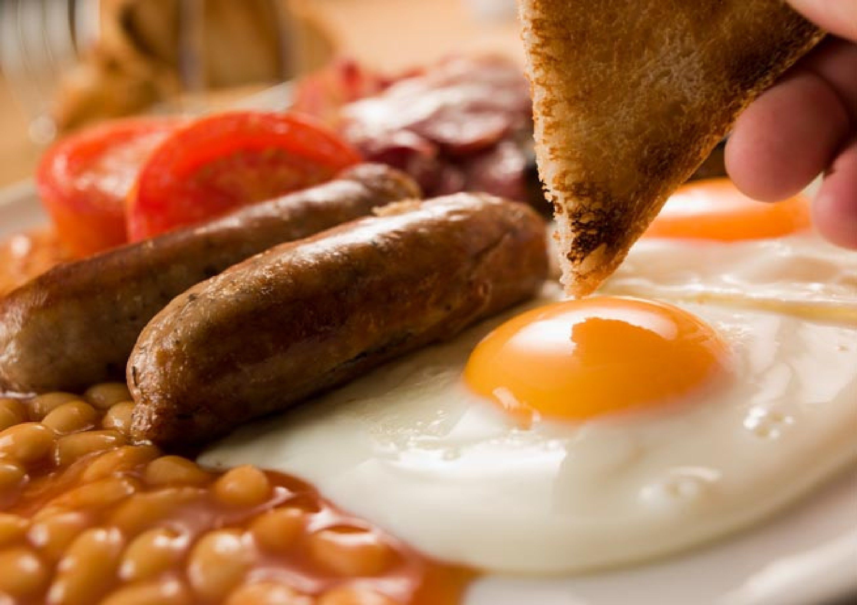 A breakfast plate with sausages, eggs, beans, and tomatoes.