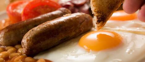 A breakfast plate with sausages, eggs, beans, and tomatoes.