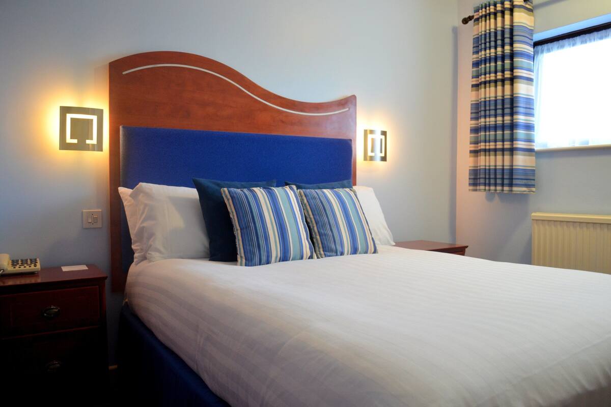 A neatly made bed with white and striped bedding, a wooden headboard, and two bedside lamps.