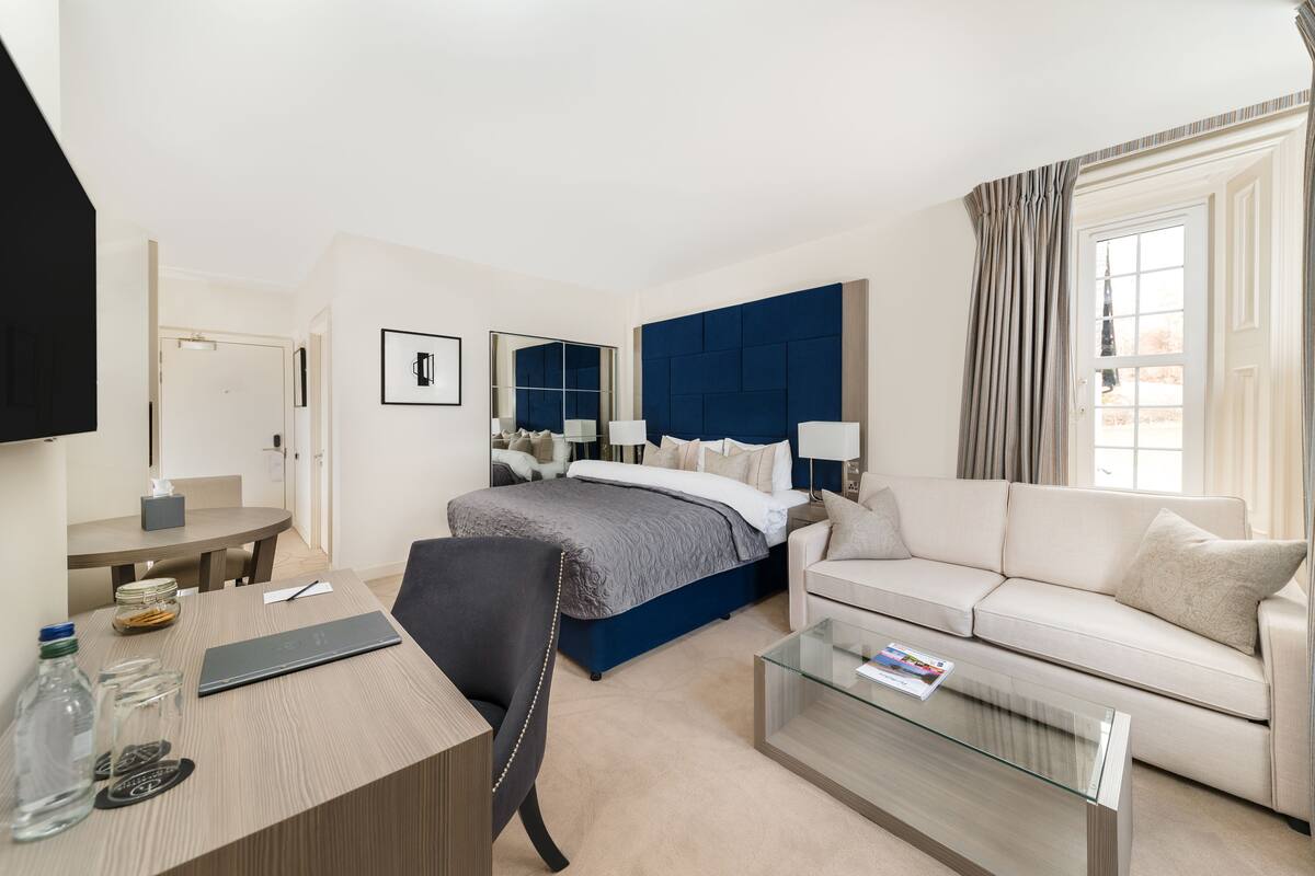 Quarto de hotel com cama, sofá, escrivaninha e mesa de centro de vidro.