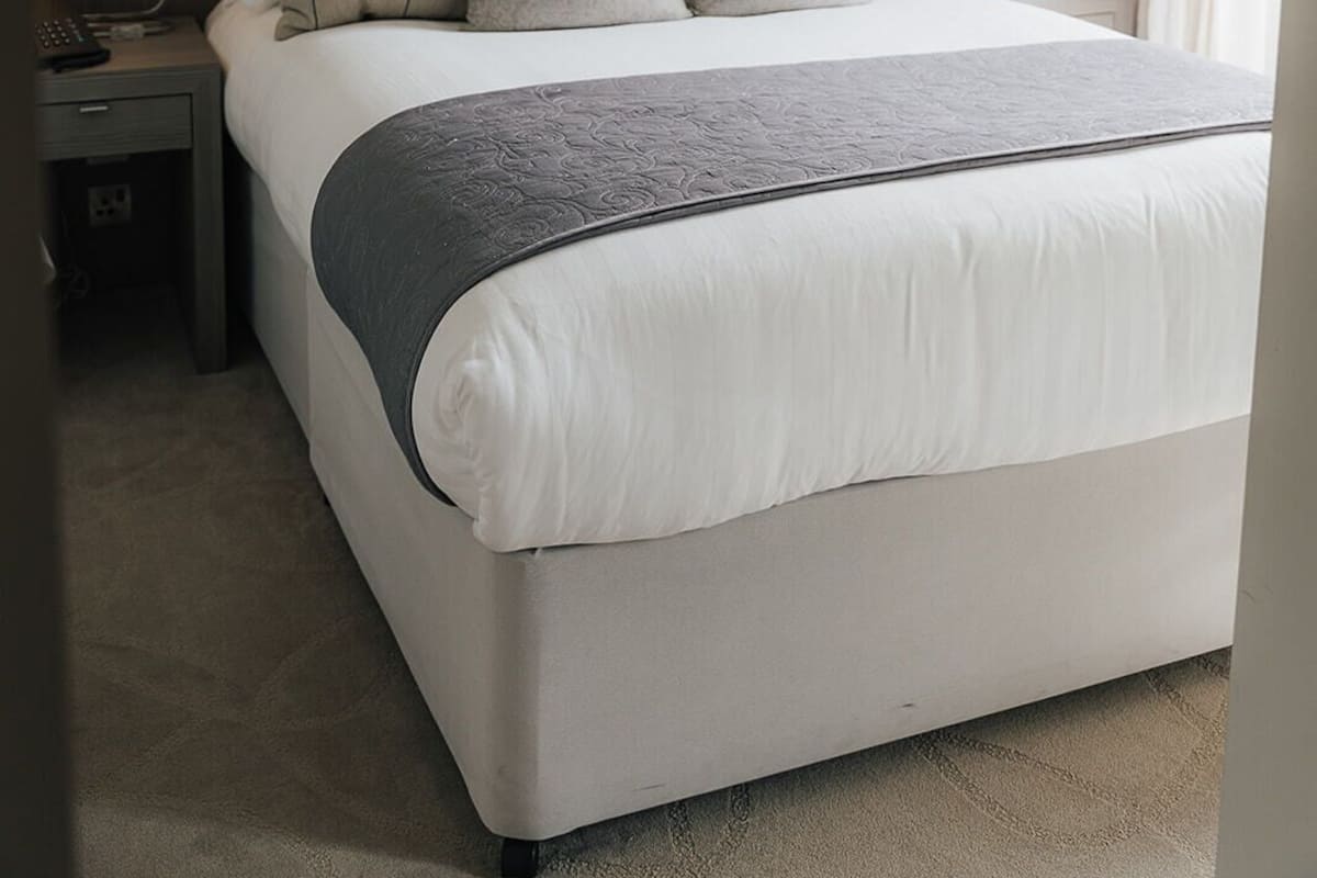 Quarto de hotel com uma cama grande, duas mesas de cabeceira com abajures, uma cabeceira e uma janela com cortinas.