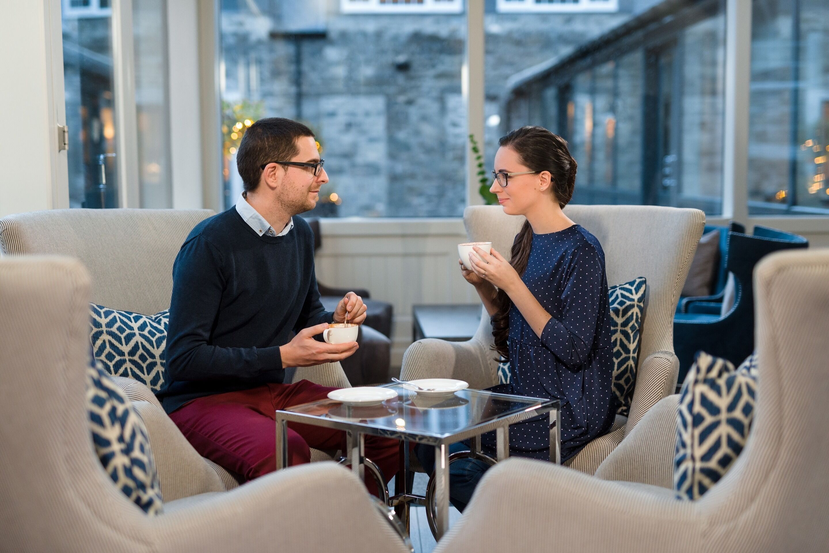 Two people sitting on a sofa in a modern room with a glass table in front of them.