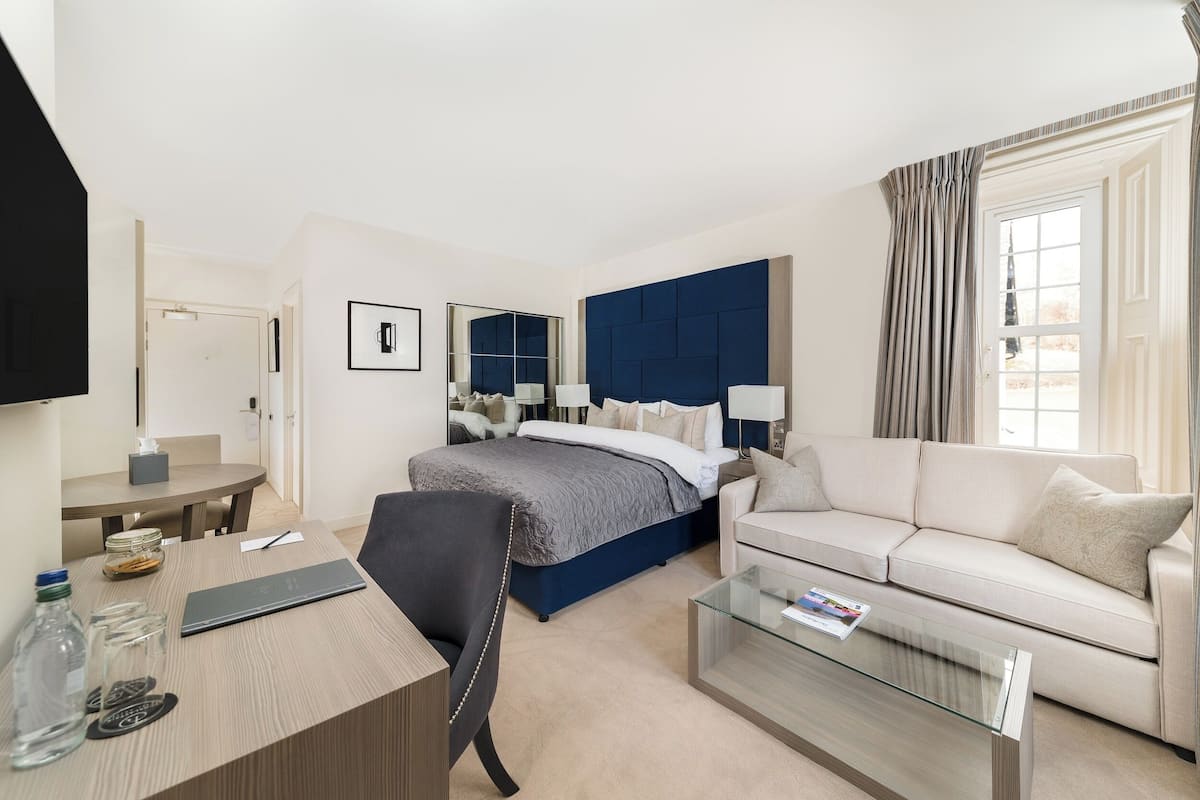 Une chambre d’hôtel comprenant un lit, un canapé, un bureau, une chaise, une table basse en verre et un miroir.