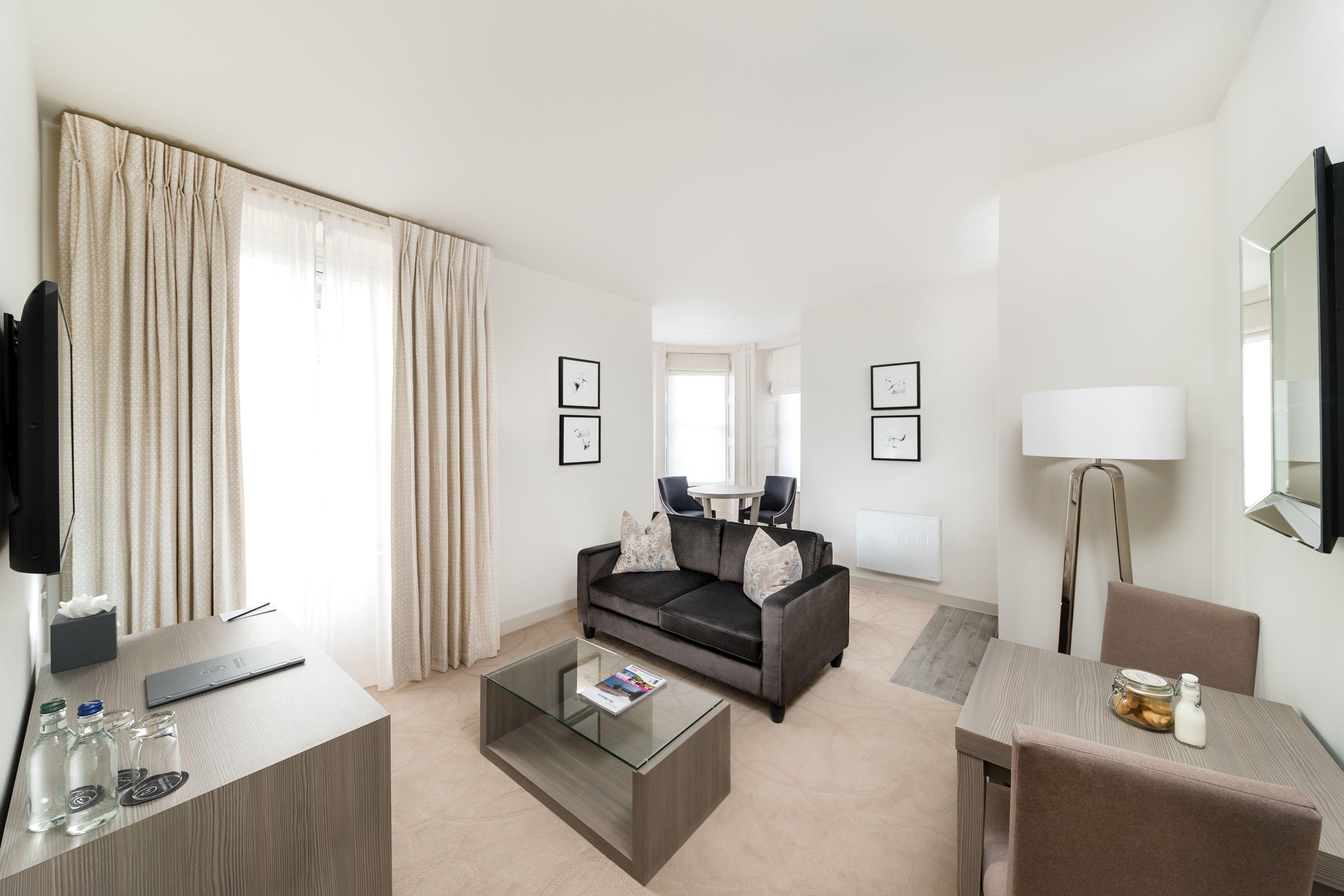 Een moderne hotelkamer met een bank, salontafel en een zithoek met stoelen en een lamp.