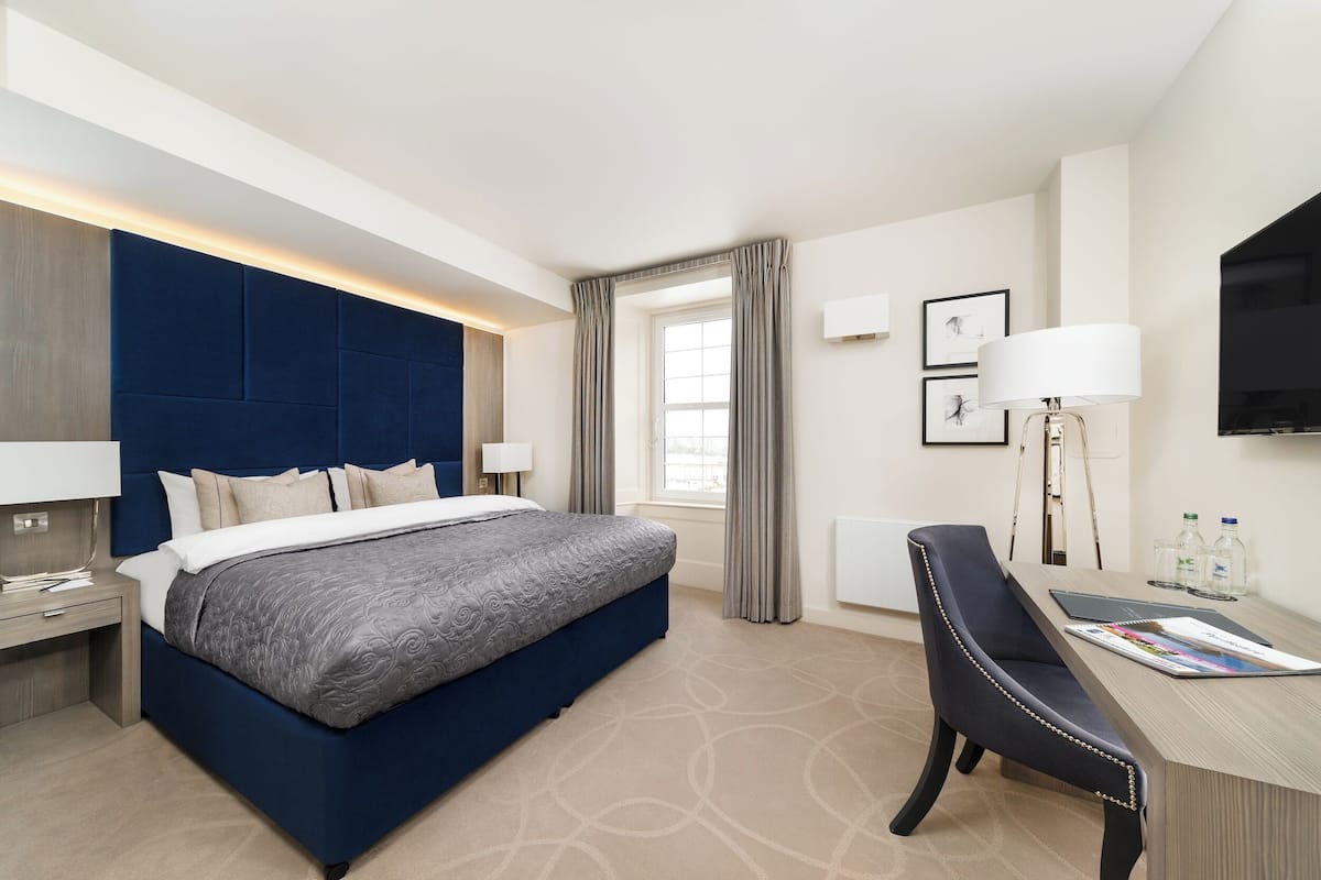 Ein Hotelzimmer mit einem großen Bett, einem Schreibtisch mit Stuhl, einem Flachbildfernseher und einem Fenster mit Vorhängen.
