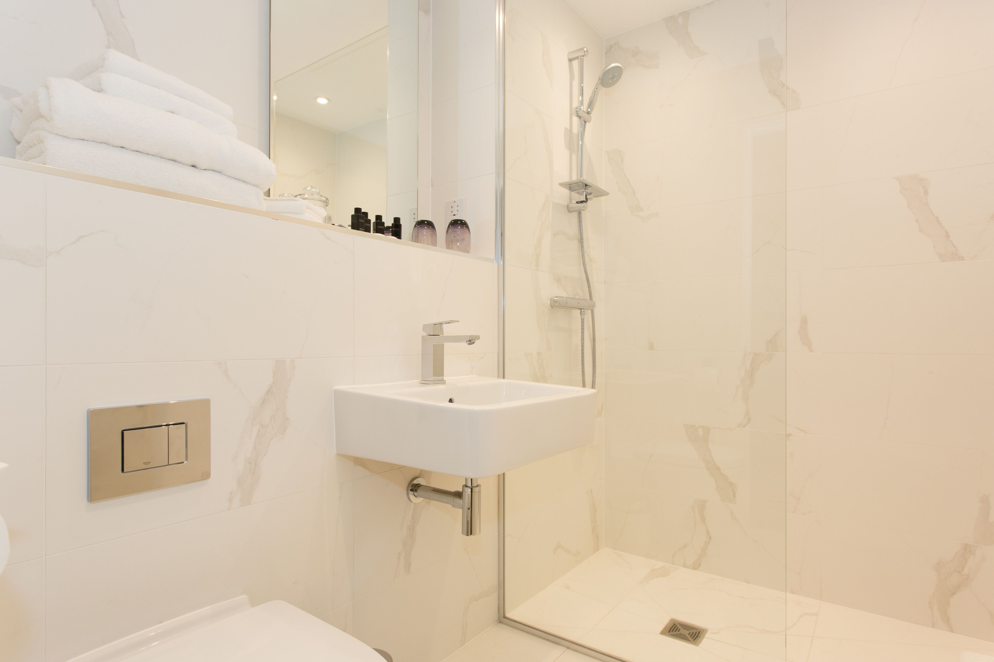 A modern bathroom with a white sink, a glass-enclosed shower, and a marble-tiled wall.