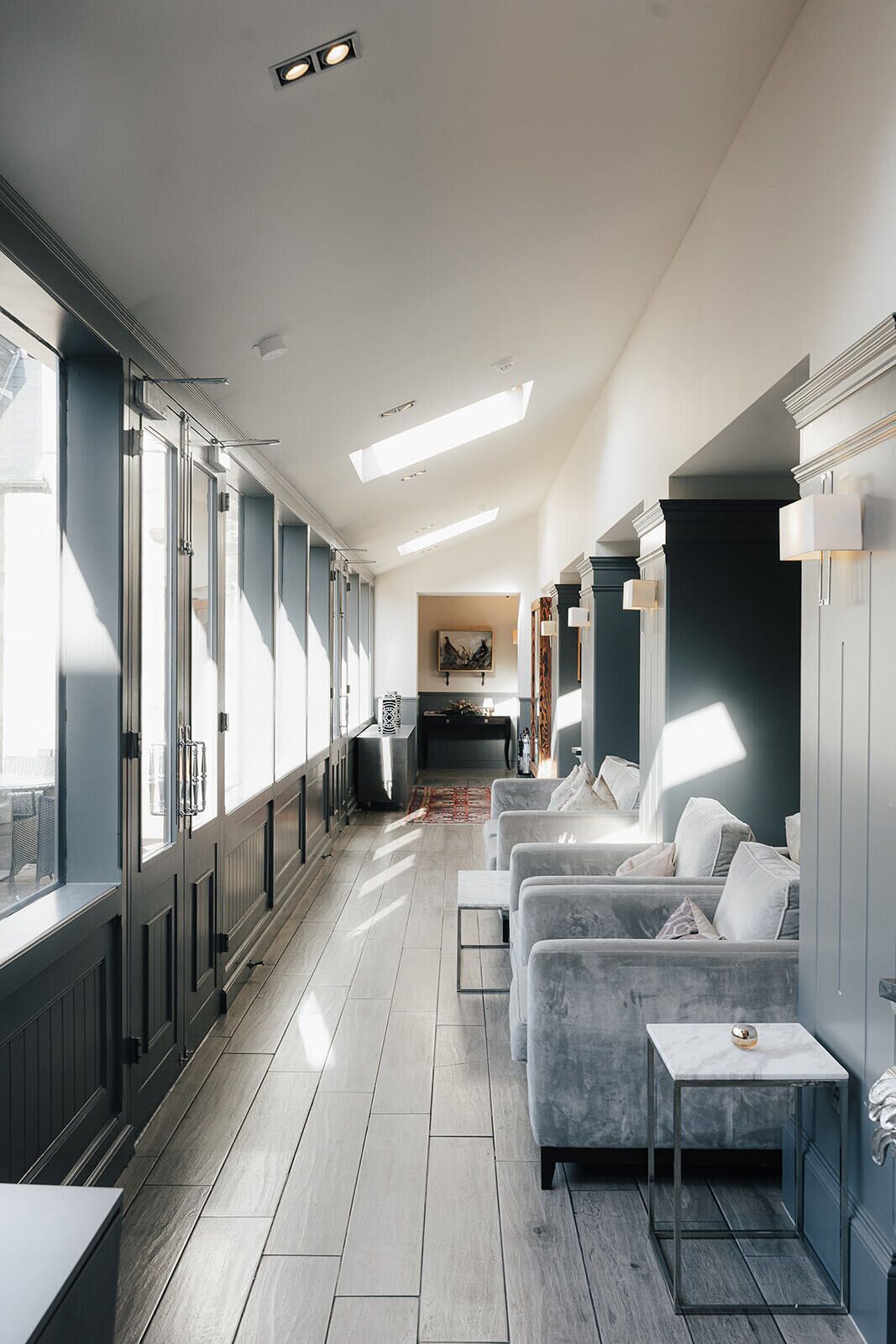 A modern hotel room with a long hallway, large windows, a sofa set, and a dining area.