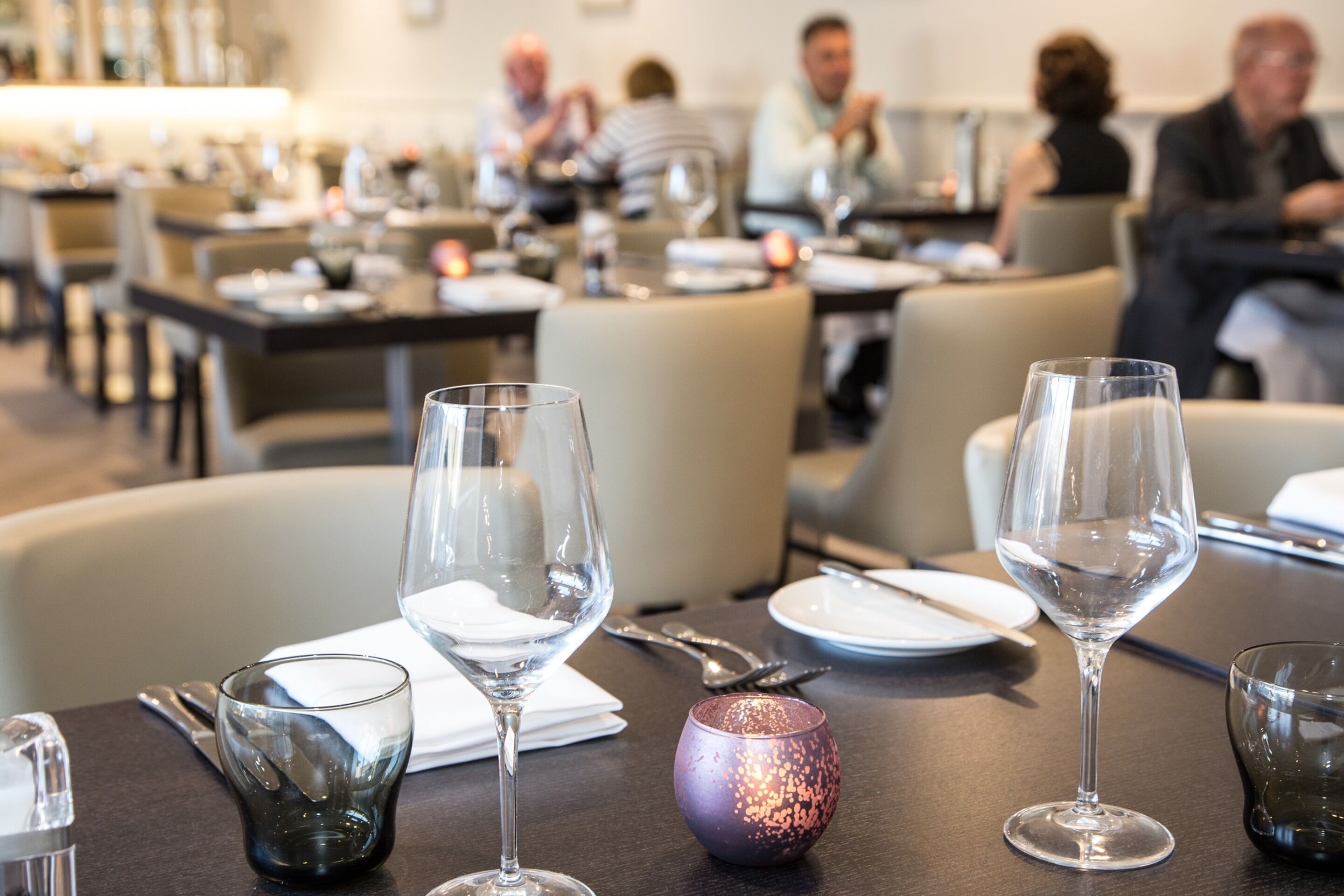 A dining area with tables set for a meal, including wine glasses, plates, and cutlery.
