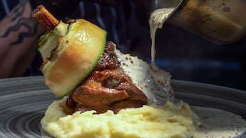 A plate with mashed potatoes, a piece of meat, and a slice of bread topped with a sauce being poured over it.