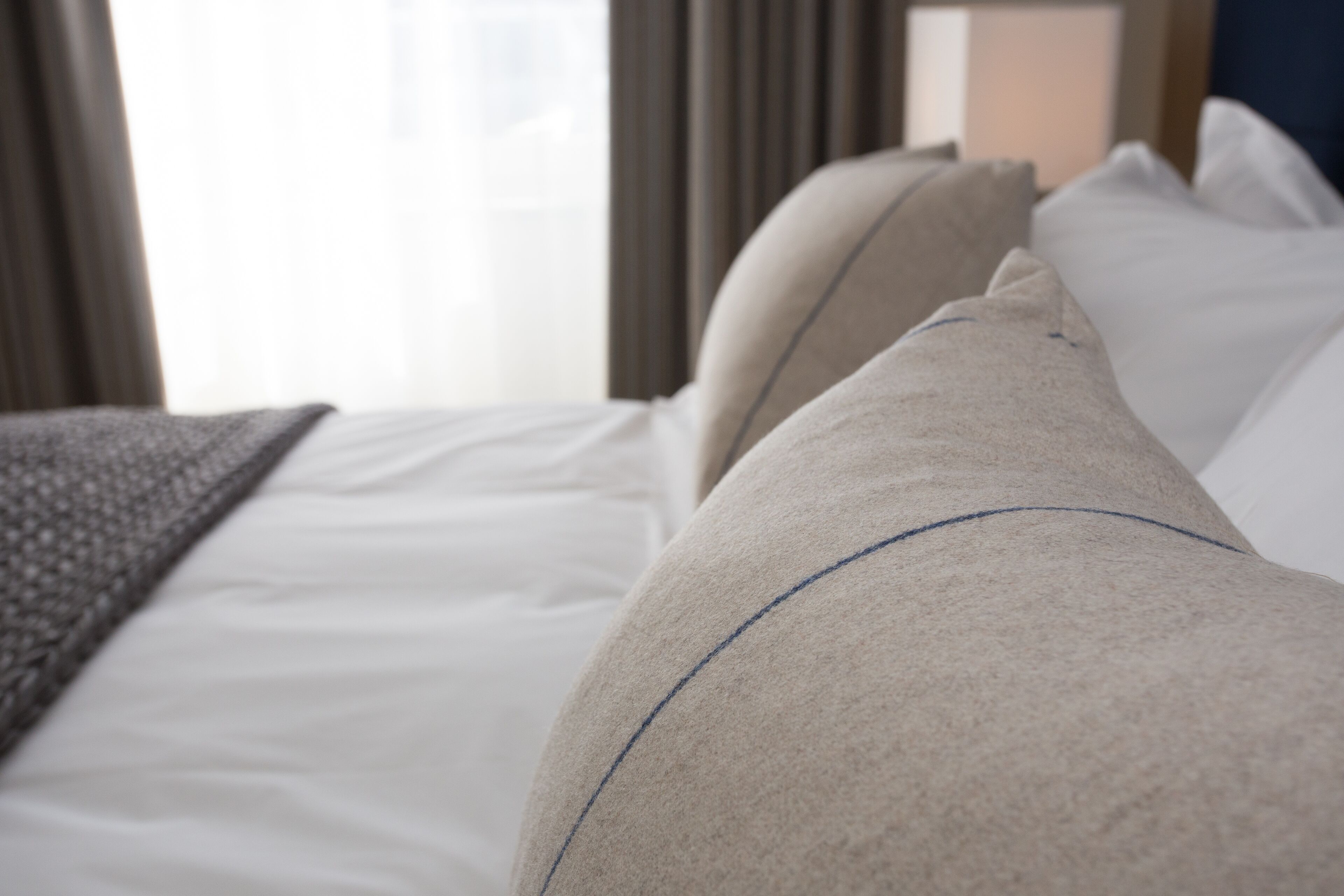 A bed with a white sheet and a beige pillow with a blue line.