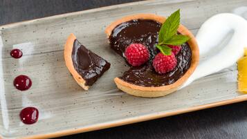 Un plato de postre con tarta de chocolate, frambuesas y una hoja de menta.