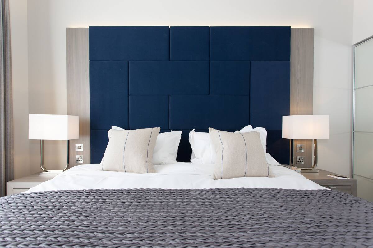 Quarto de hotel moderno com uma cama grande, duas luminárias de cabeceira e um painel de cabeceira escuro.