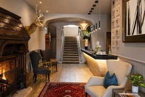 A spacious living room with a fireplace, a staircase, and a kitchen area. - Dunalastair Hotel Suites (Pitlochry)
