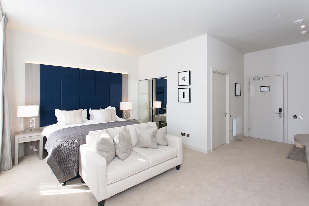 Quarto moderno com uma cama grande, um sofá branco, uma mesa de cabeceira com abajur, um espelho e quadros nas paredes.