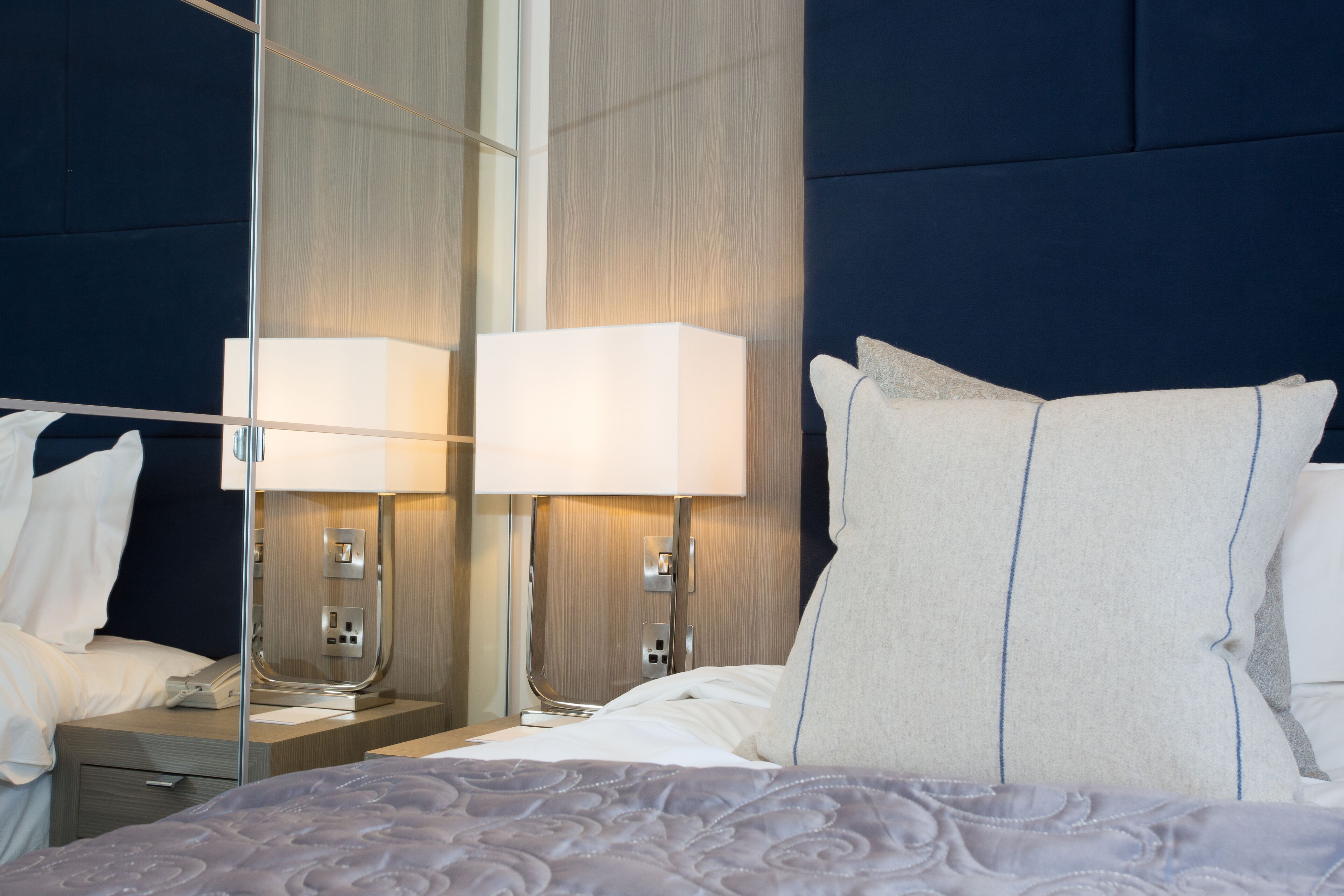 A hotel room with a large bed, two bedside lamps, a nightstand, and a mirror.