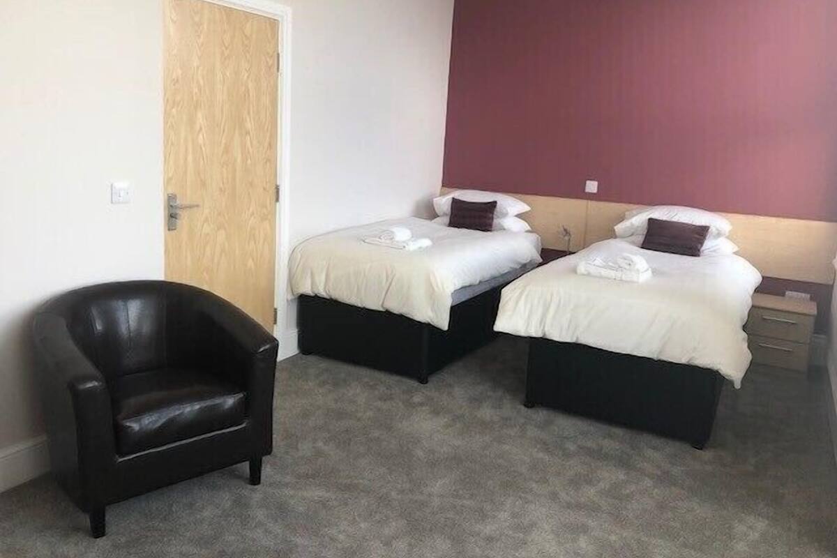 A hotel room with two single beds, a black leather chair, and a wooden door.