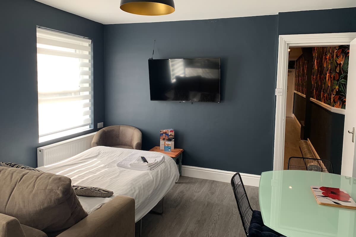 A modern bedroom with a bed, a chair, a TV, and a glass table.