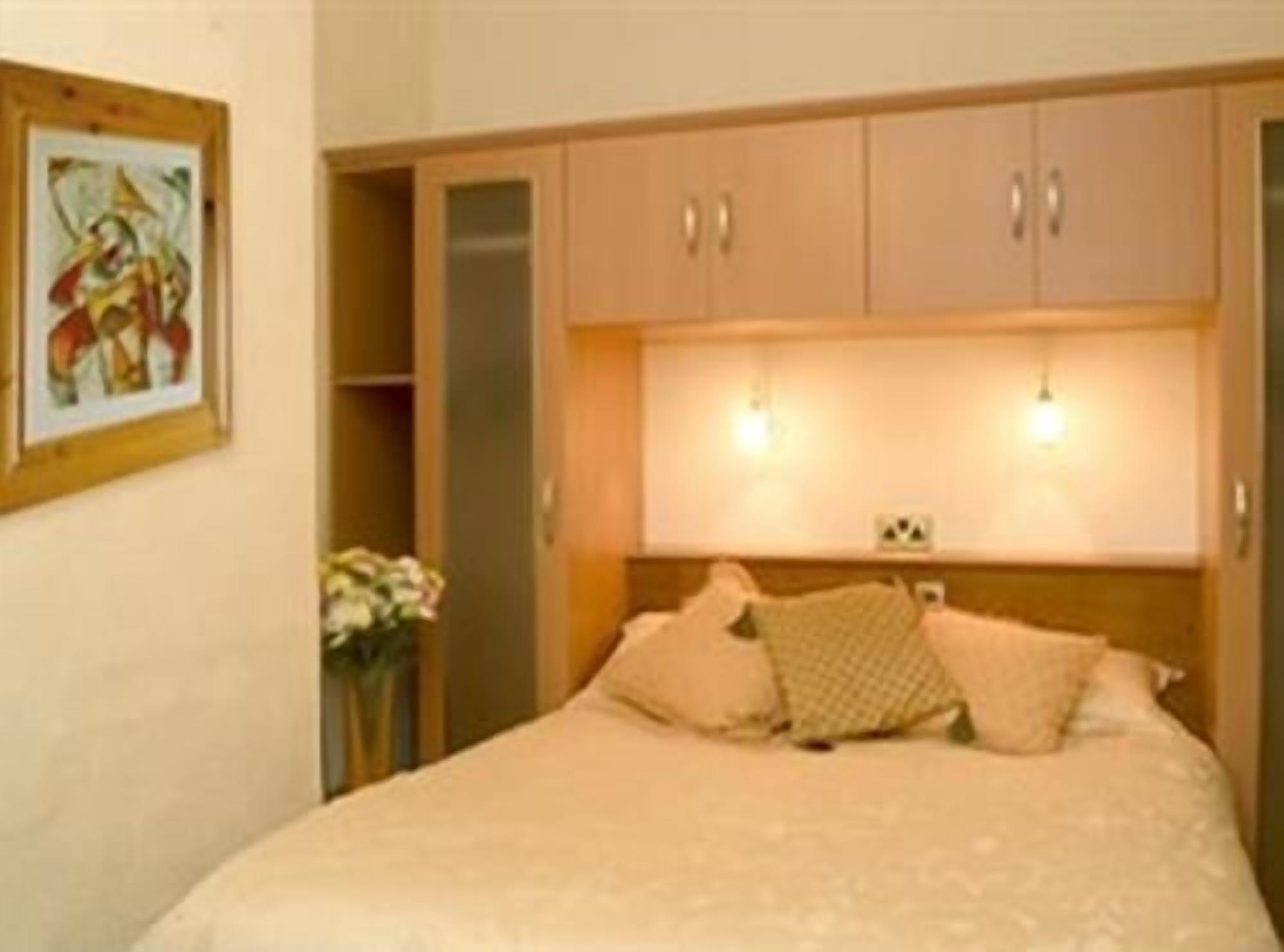 A bedroom with a bed, a nightstand, a lamp, a painting on the wall, and a cabinet.