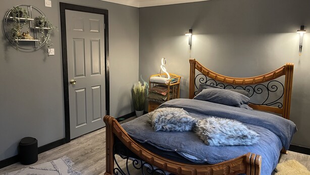 Un dormitorio con cama de madera, paredes grises, una puerta y una lámpara fijada a la pared.