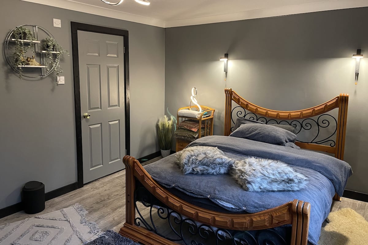 Un dormitorio con cama de madera, paredes grises, una puerta y una lámpara fijada a la pared.