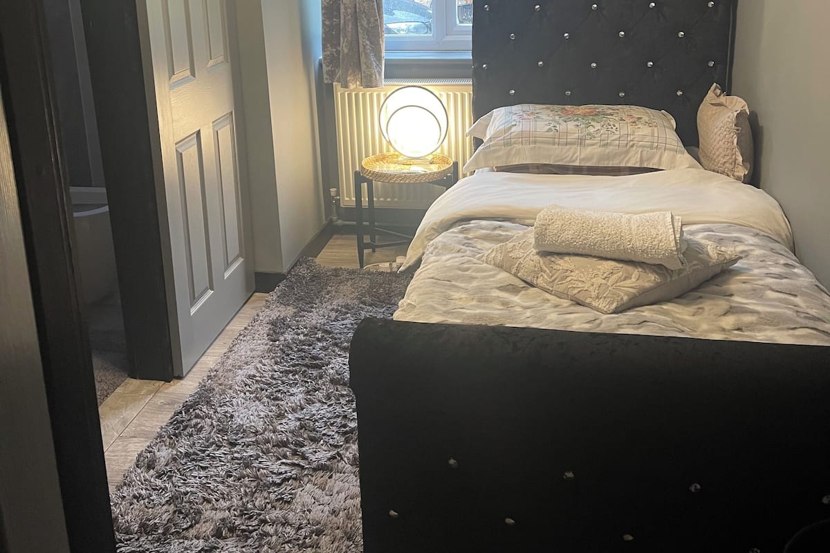 Un dormitorio con cama, ventana con cortinas, radiador y puerta.