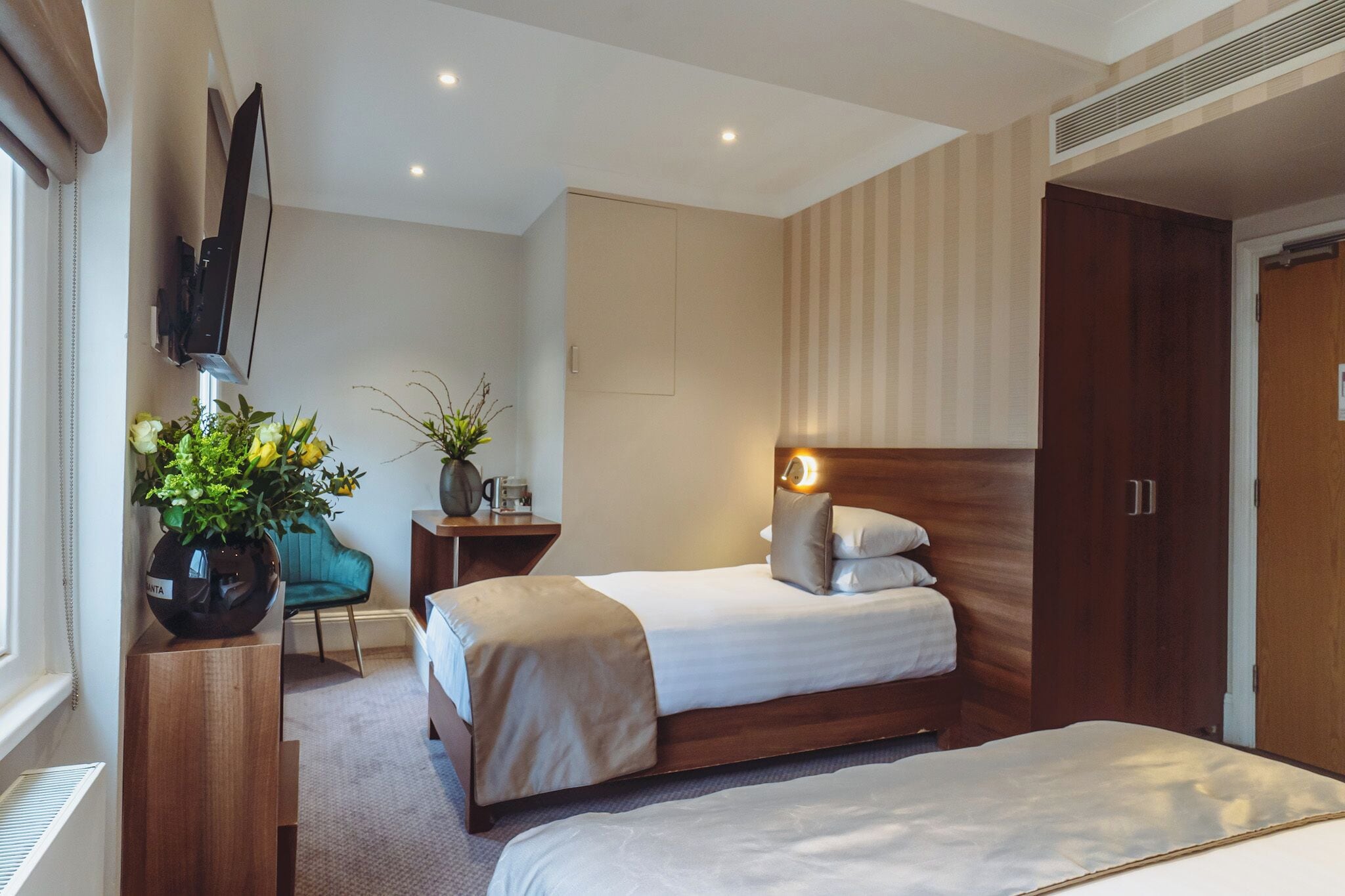 A hotel room with a bed, a desk, a chair, a TV, and a wardrobe.