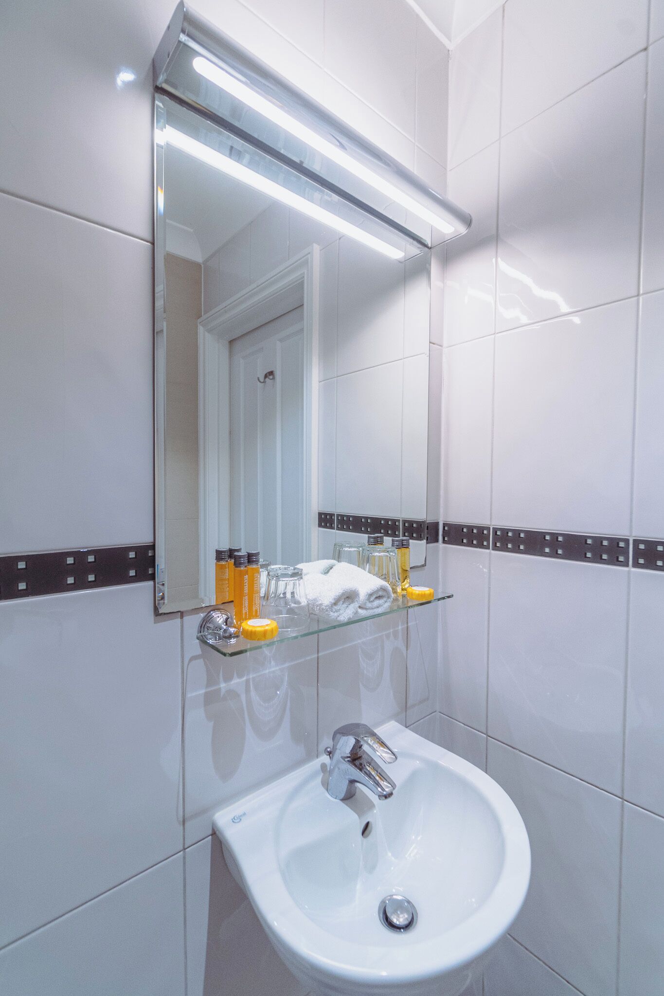 A bathroom with a white sink, a mirror, and a glass shelf with toiletries.