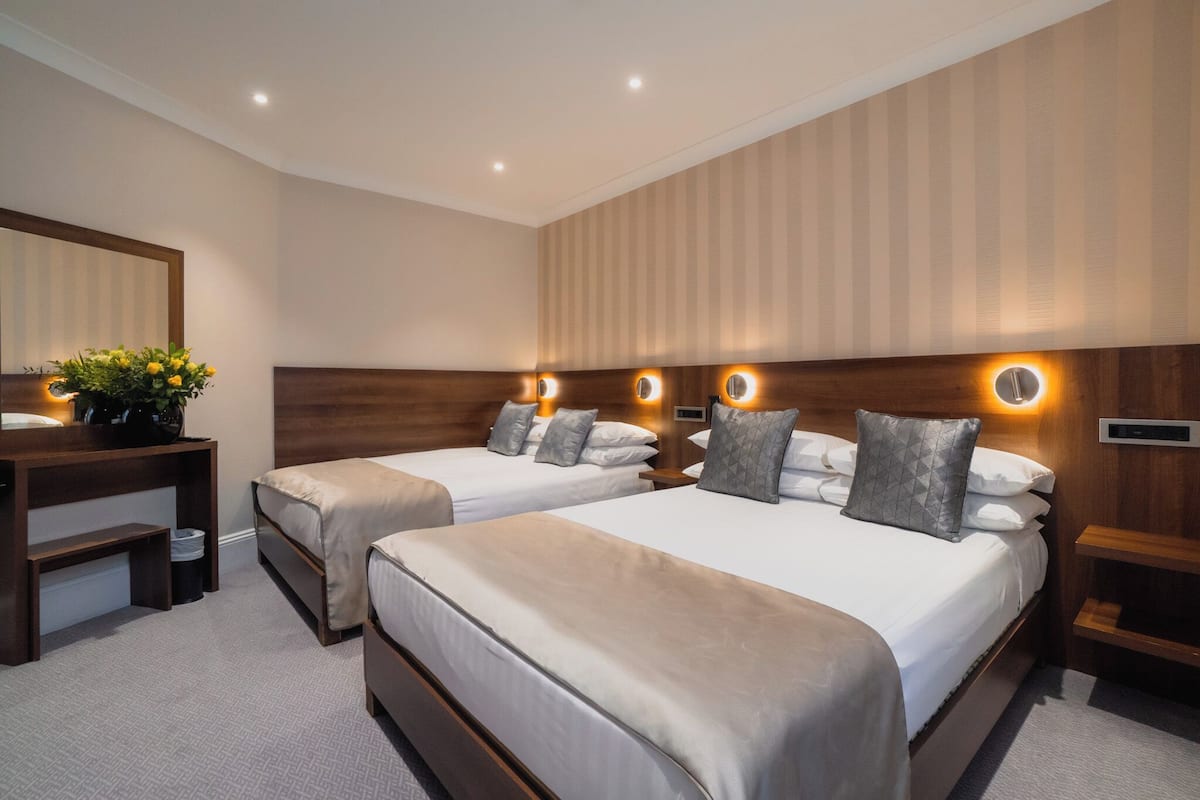 A hotel room with two beds, a desk, and a mirror.