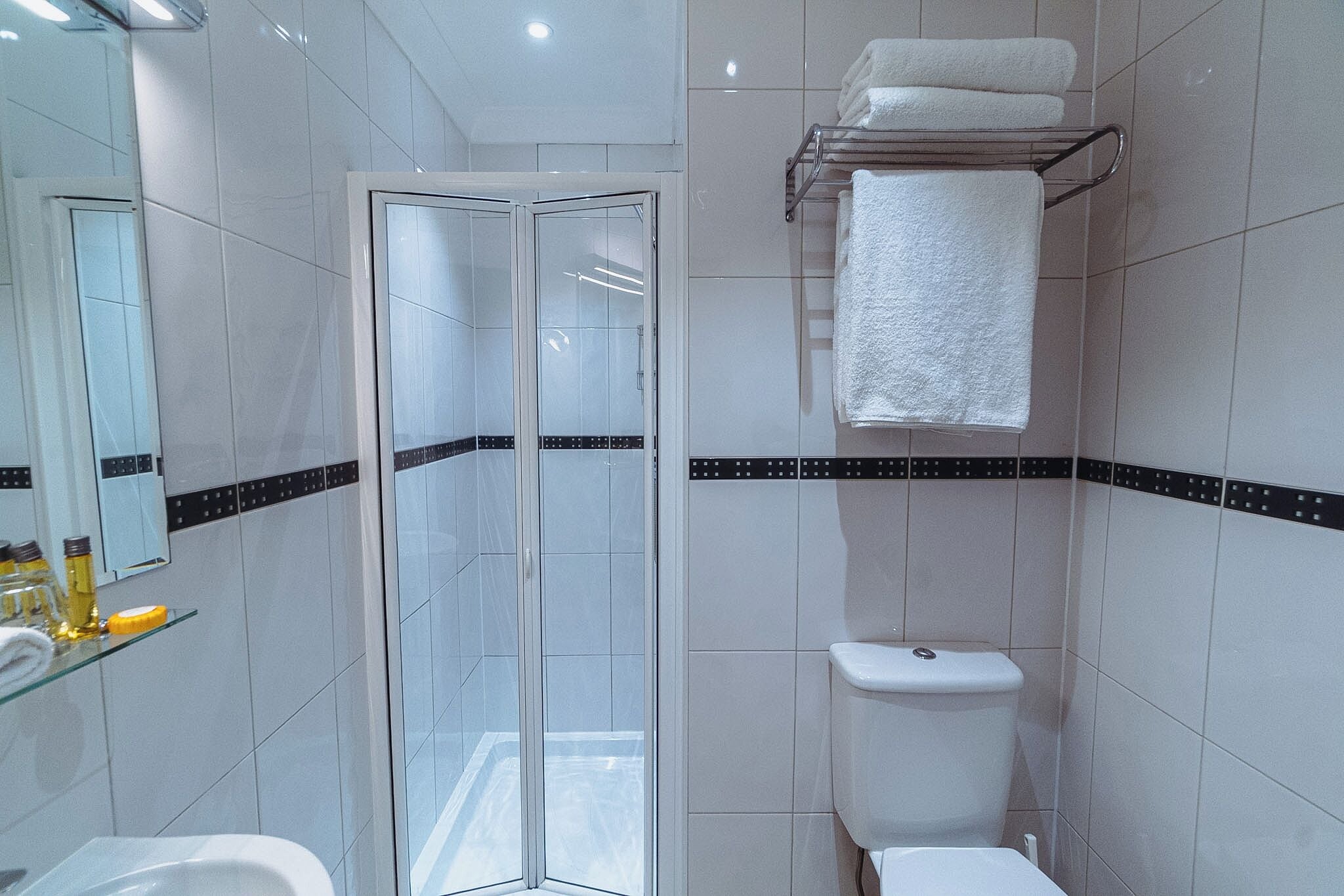 Une salle de bain moderne avec une douche à parois de verre, des toilettes et une étagère en verre où sont rangés les articles de toilette.