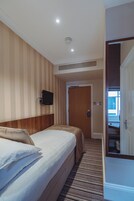 A hotel room with a bed, a television mounted on the wall, a door, and a carpeted floor.