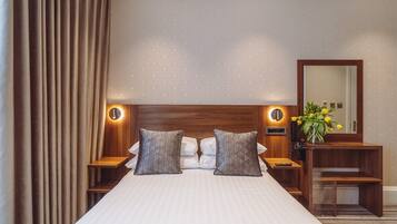 A hotel room with a large bed, two bedside tables with lamps, a nightstand, a mirror, and a vase with flowers.