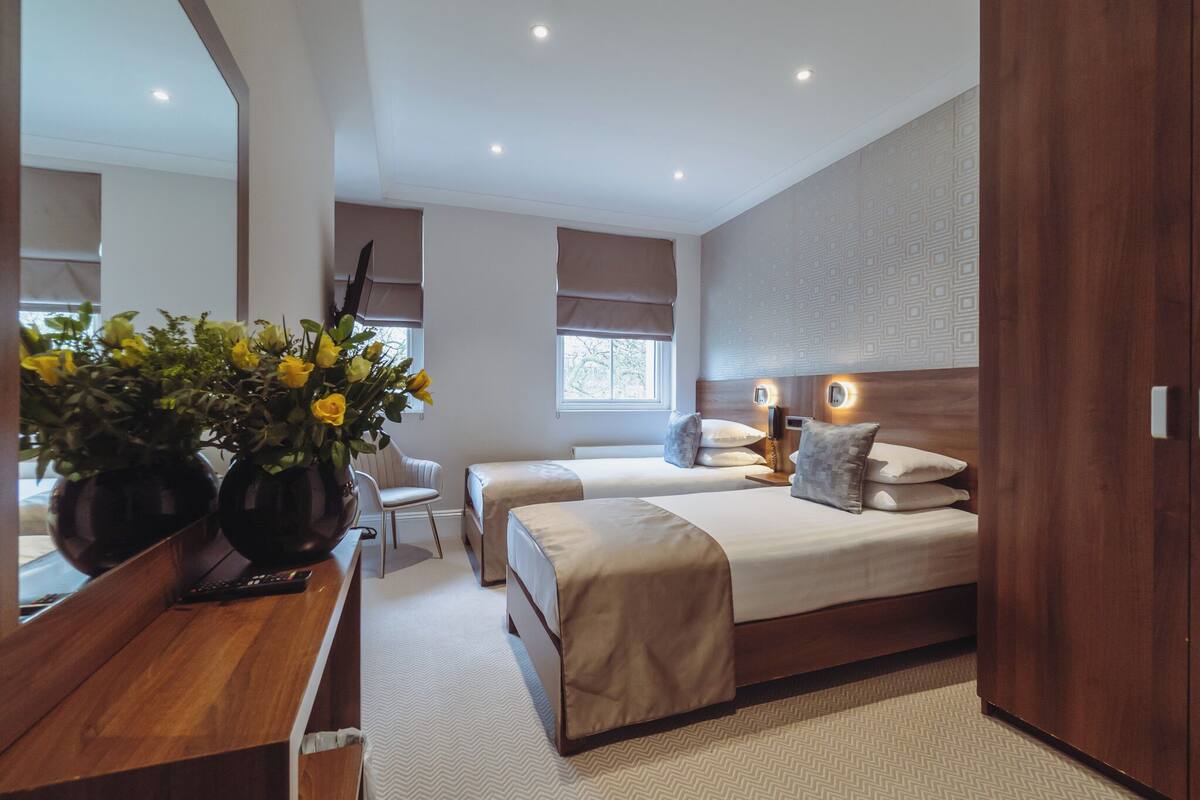 A modern hotel room with two beds, a wooden desk, and a large mirror.