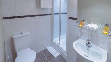 Une salle de bain comprenant des toilettes, une douche en verre, un lavabo et une étagère avec des articles de toilette.