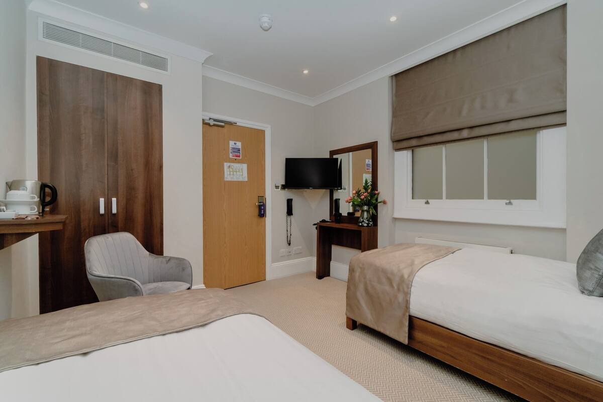 A hotel room with a bed, a chair, a desk with a coffee maker, a TV, and a large window with a view.