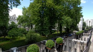 Un balcon agrémenté de plantes en pot, une vue sur un parking et des bâtiments en arrière-plan.
