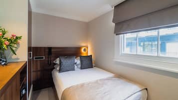 A compact hotel room with a bed, bedside table, and a window with a view of buildings.