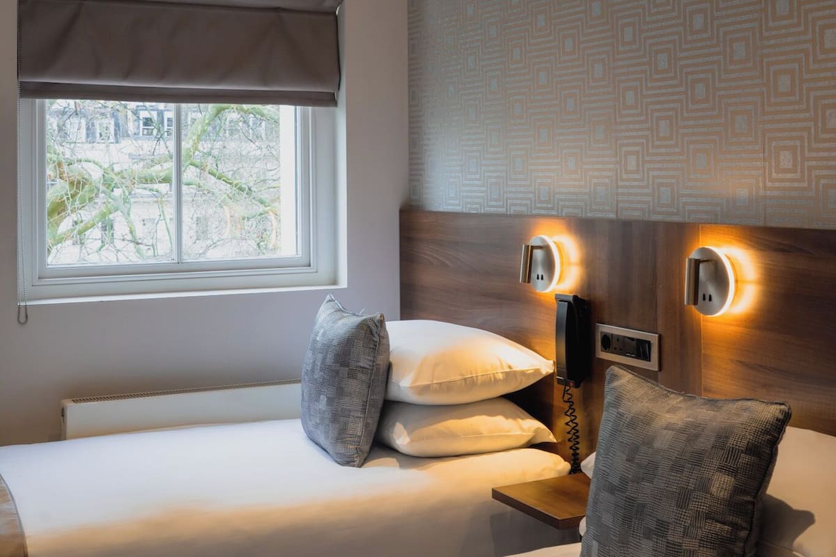 A hotel room with a bed, two bedside tables, a window with a view, and a patterned wall.