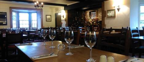 A restaurant interior with multiple tables, each set with wine glasses, cutlery, and salt shakers.