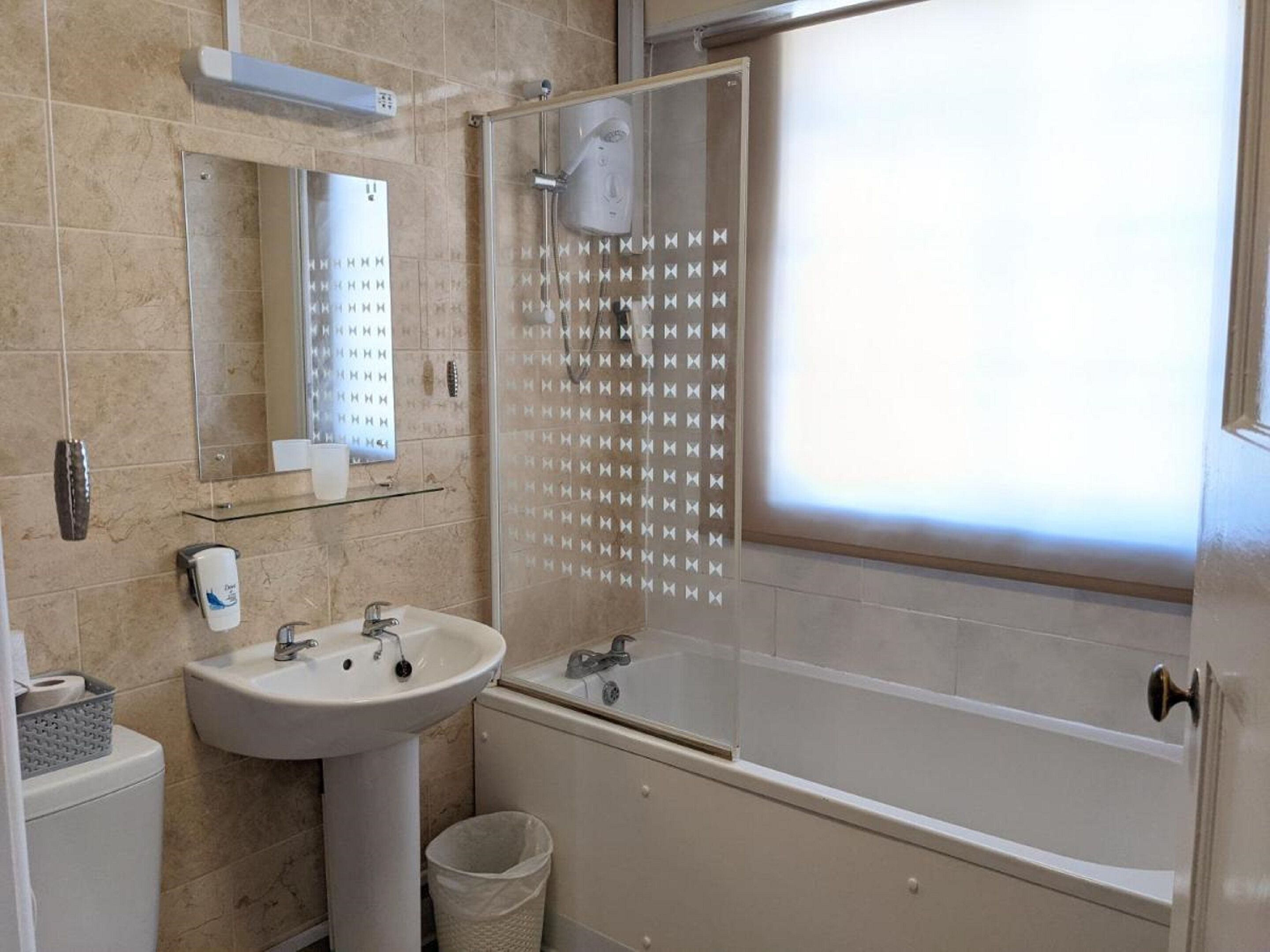 A bathroom with a sink, mirror, shower, and a window with a frosted glass door.