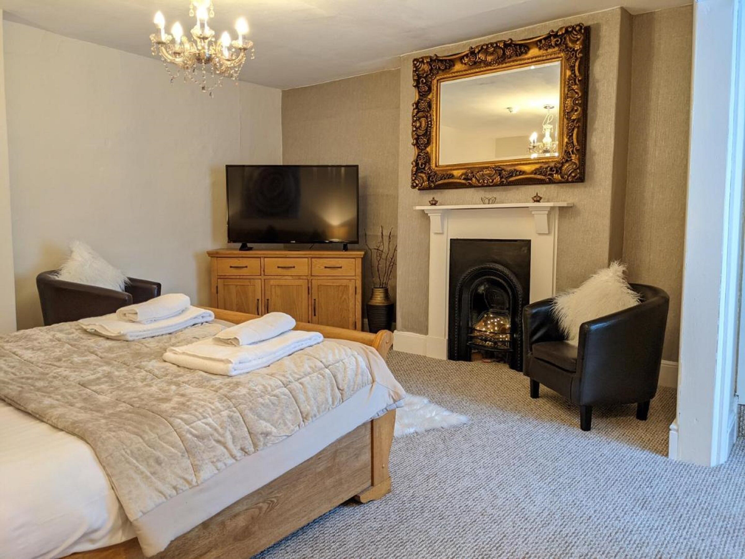 A hotel bedroom with a large bed, a television, a fireplace, and a mirror.