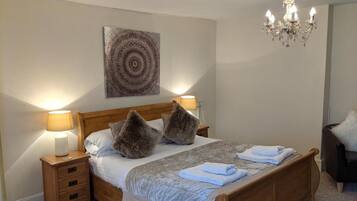 Een netjes ingerichte slaapkamer met een houten bed, twee bedlampen, een kroonluchter en een kunstwerk aan de muur.
