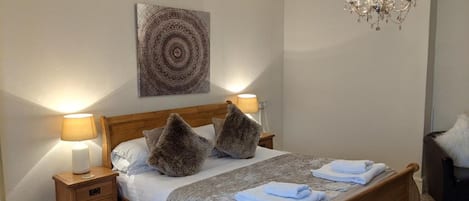 A neatly arranged bedroom with a wooden bed, two bedside lamps, a chandelier, and a wall art piece.