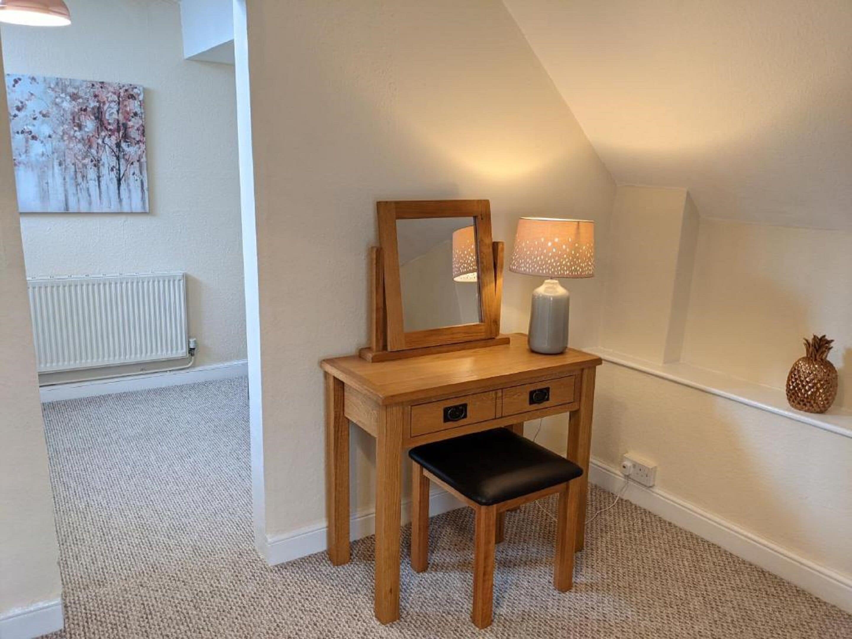 A small, cozy room with a wooden vanity, a mirror, a lamp, and a small stool.