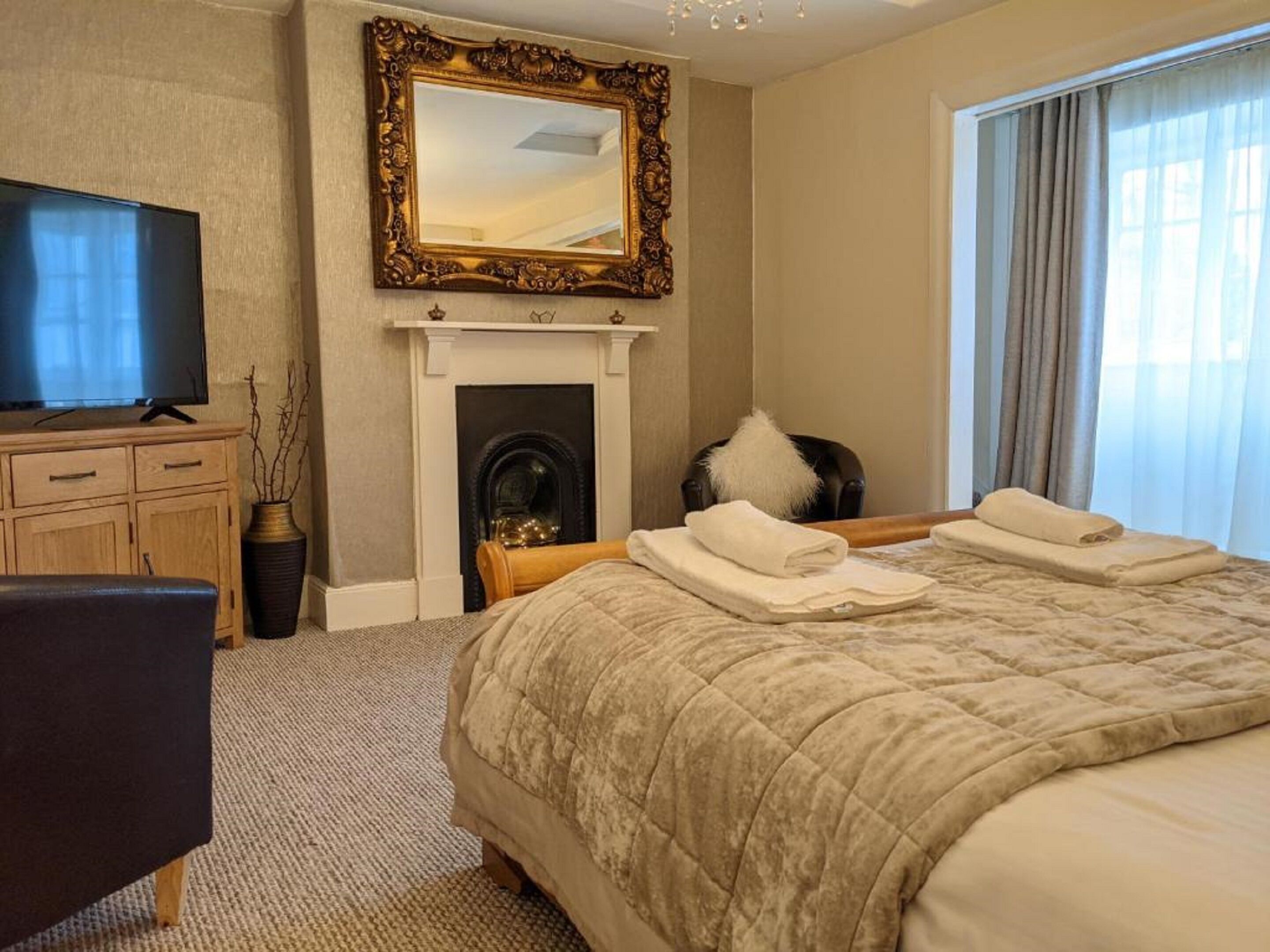 Habitación de hotel con una cama grande, televisor, chimenea y una ventana con cortinas.